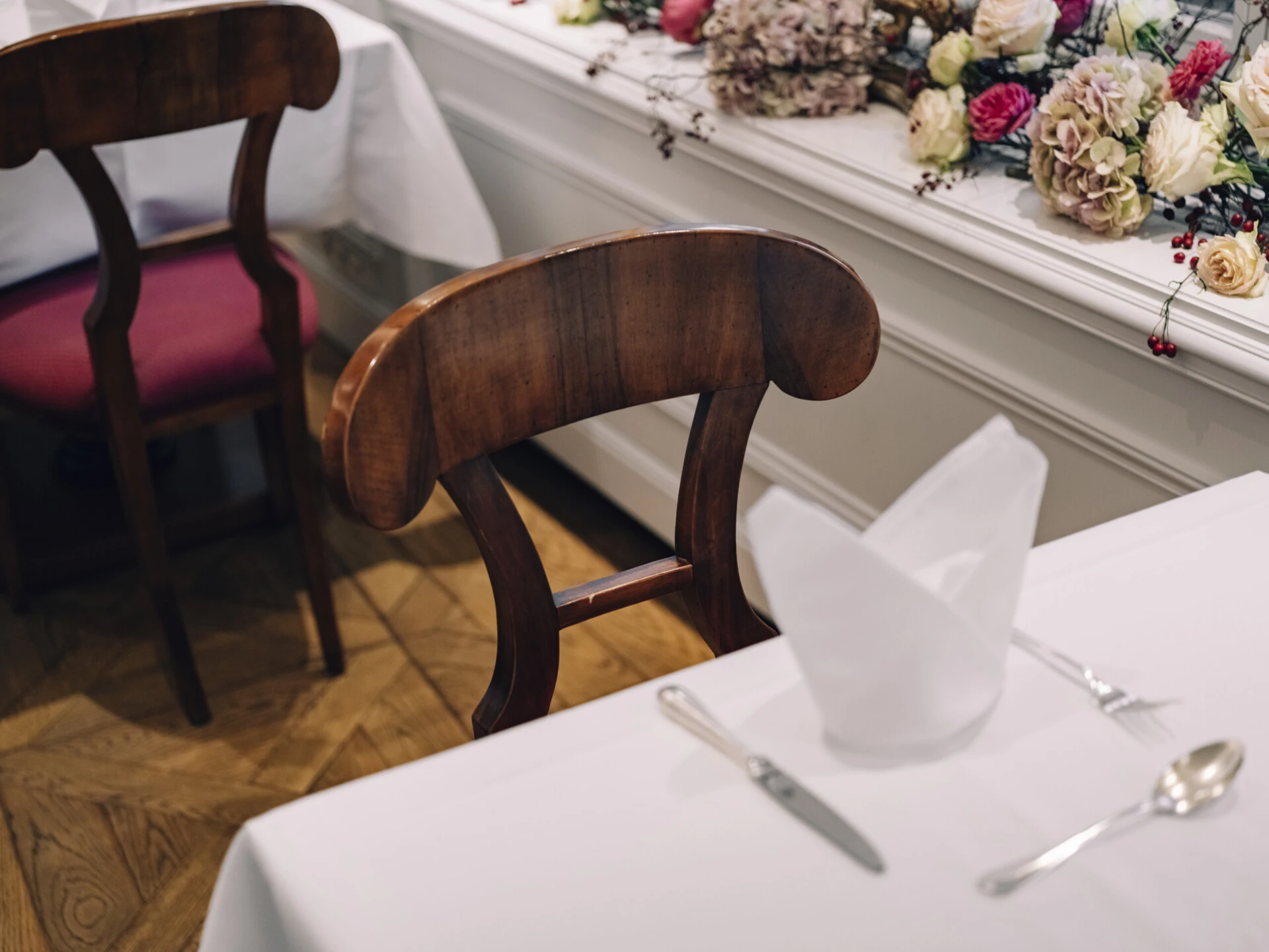 Detail of a set table with a white napkin and wooden chair.
