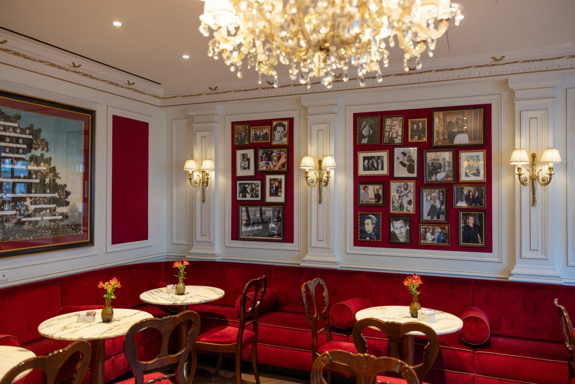 Stylish seating area with red upholstered benches, marble tables and historic photographs.