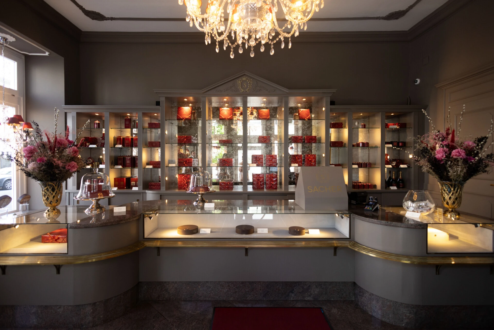 Full view of the Sacher confectionery with display counter, chandelier and floral decorations.