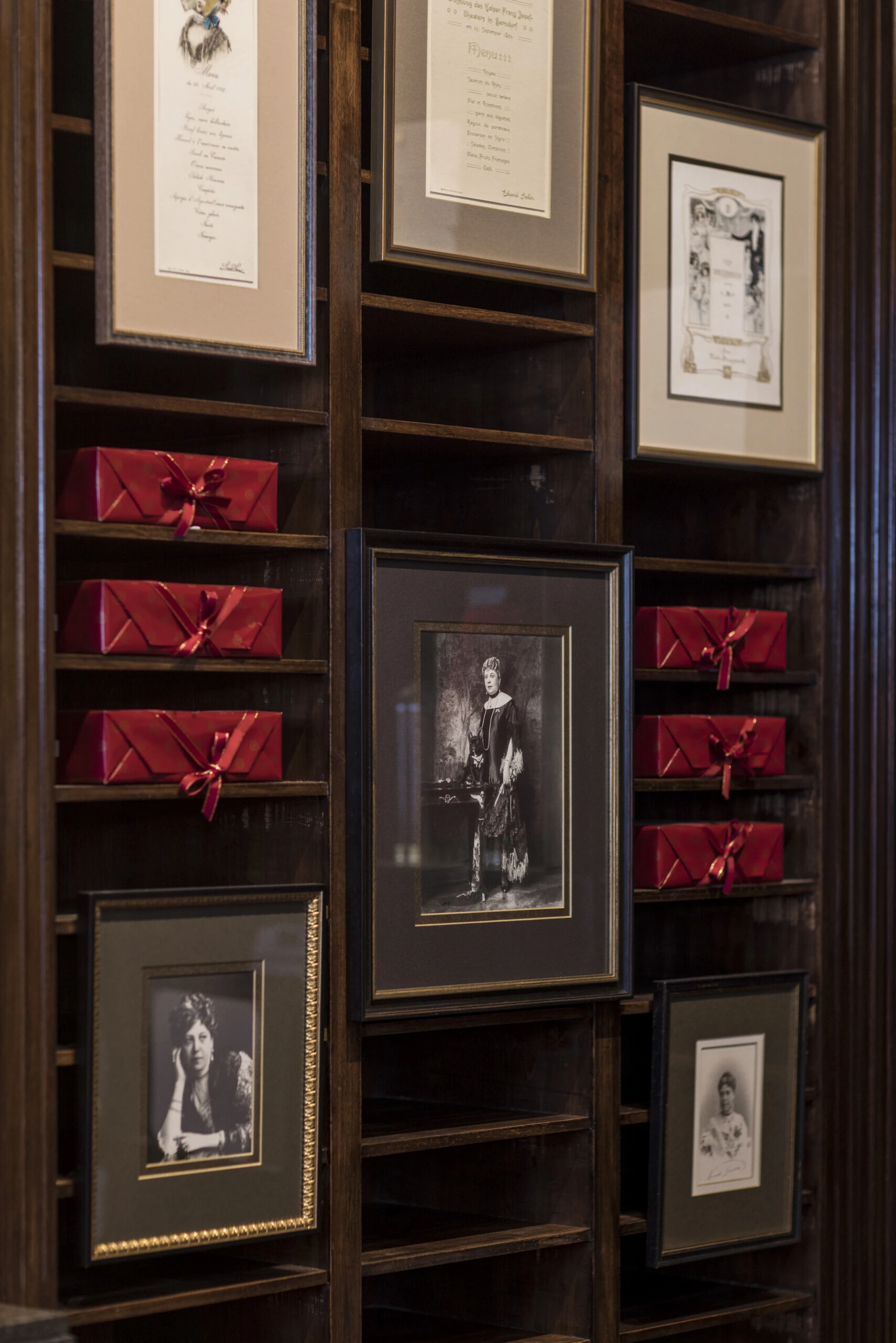 Historic photographs and red-packaged Sacher specialities displayed on dark wooden shelves.