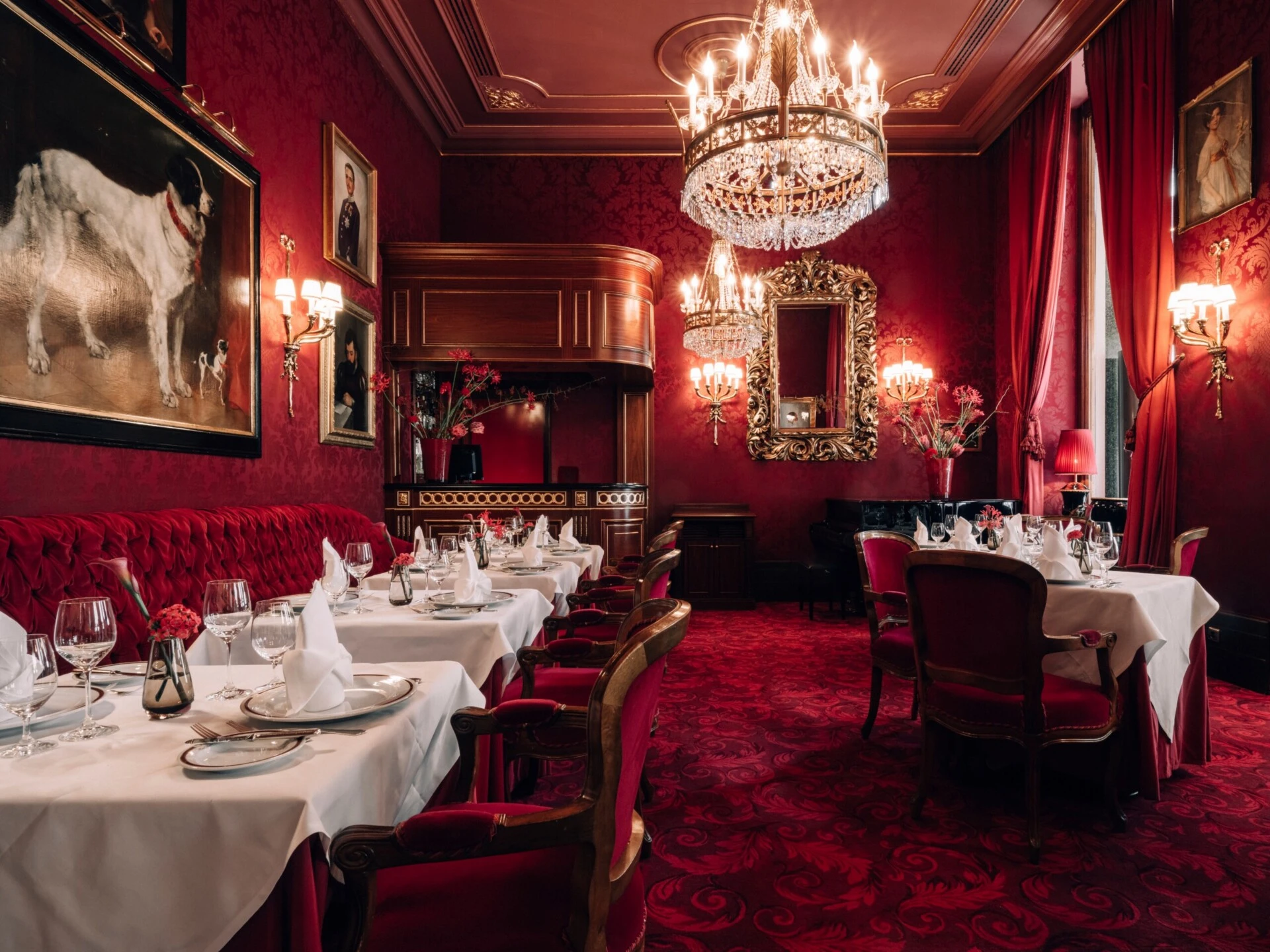 Festively set Restaurant Rote Bar at Hotel Sacher Vienna with crystal chandeliers, red velvet seating, gold chairs and white floral arrangements.
