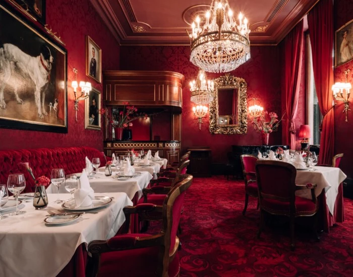 Festively set Restaurant Rote Bar at Hotel Sacher Vienna with crystal chandeliers, red velvet seating, gold chairs and white floral arrangements.
