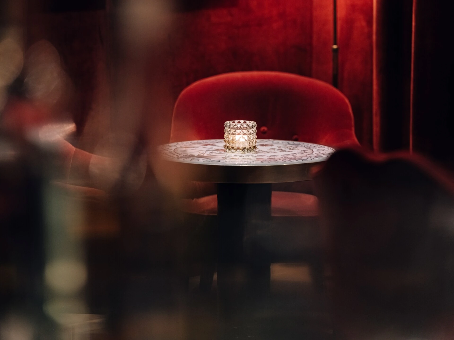 Small bar table with candlelight and a red velvet chair.