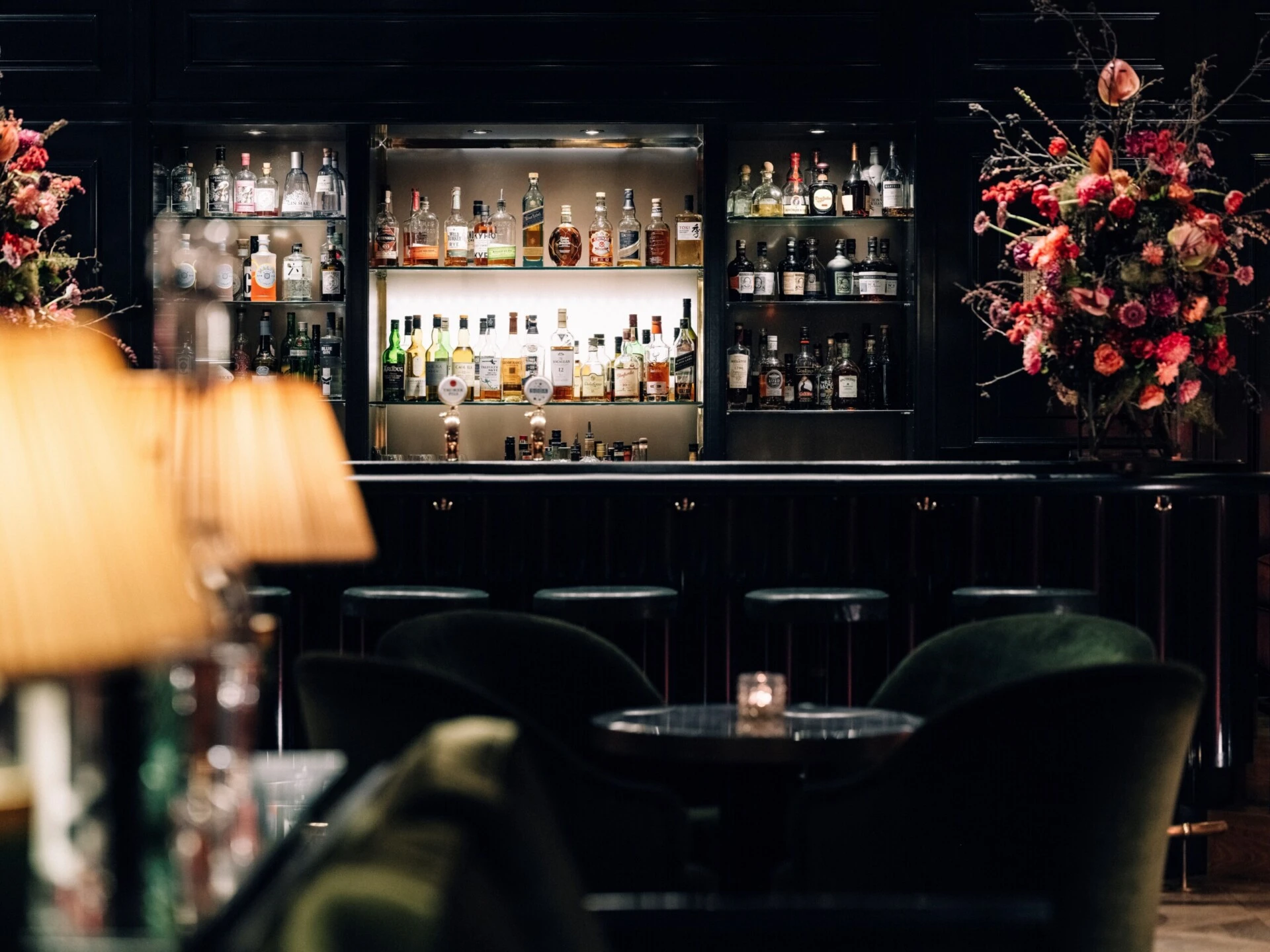 Elegant hotel bar with an illuminated bottle display and floral arrangements.