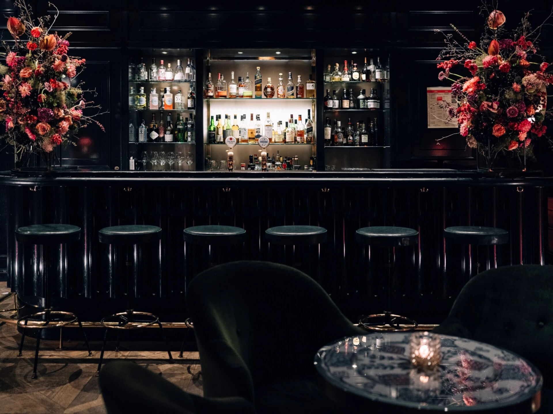 Elegant hotel bar with an illuminated bottle display and floral arrangements.