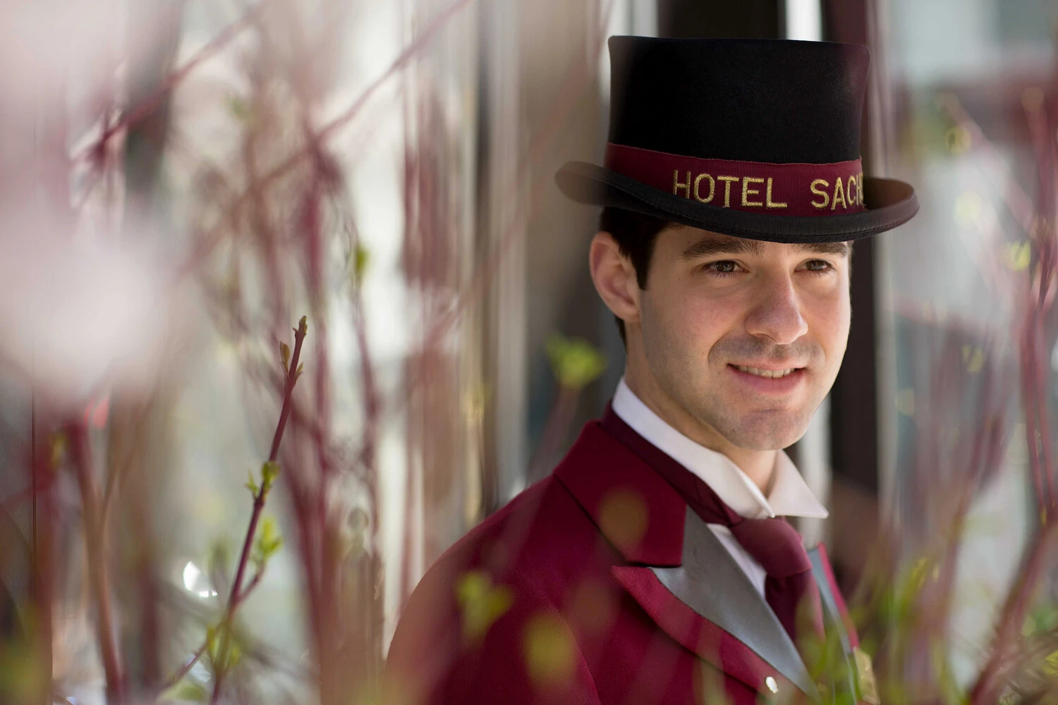 A smiling doorman in a burgundy uniform and top hat labeled 