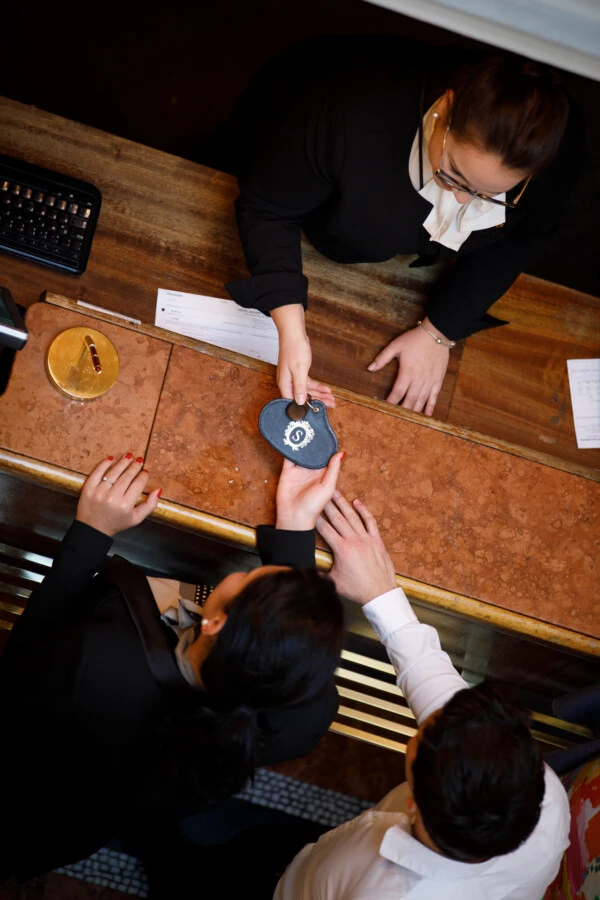 Concierge at Hotel Sacher Salzburg handing a room key to a guest at the reception desk.