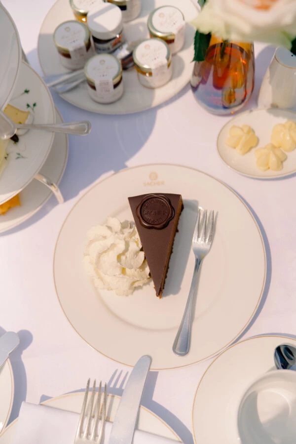 A slice of Original Sacher-Torte with whipped cream on a set table at the Hotel Sacher in Vienna.