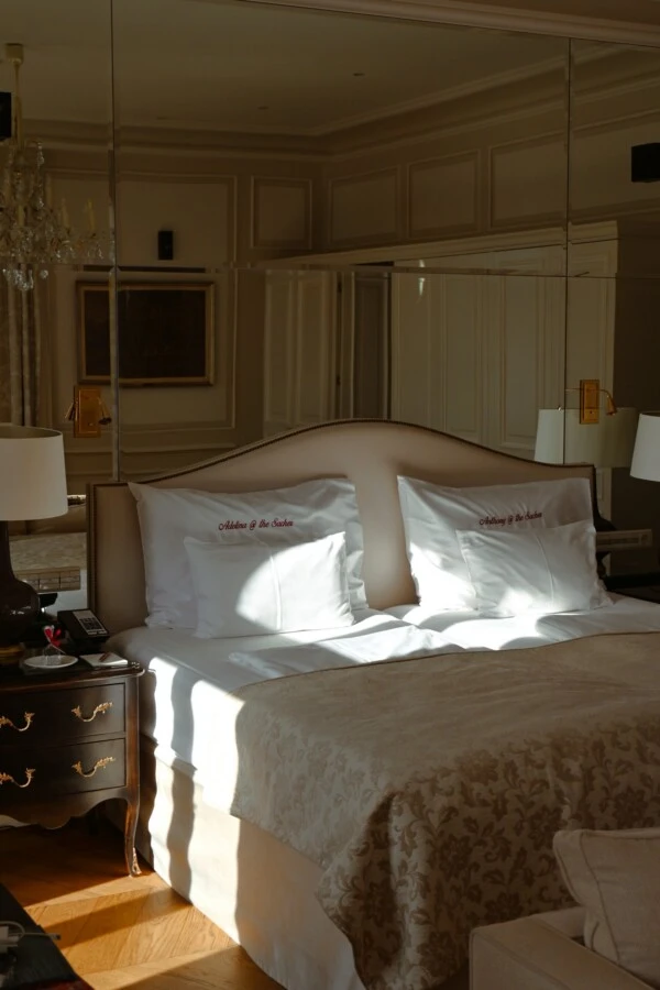 An elegant bedroom at the Hotel Sacher Vienna with a double bed, personalized pillows, and warm sunlight.