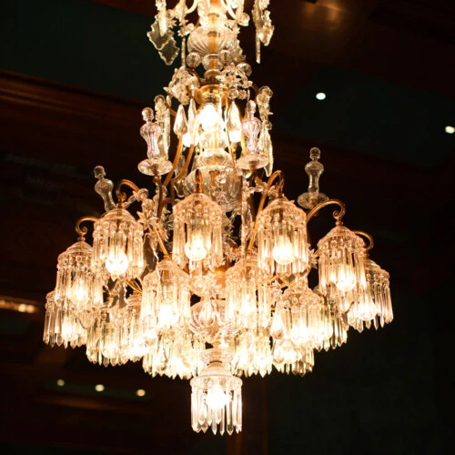 An ornate crystal chandelier glows warmly in an elegant, dimly lit room.