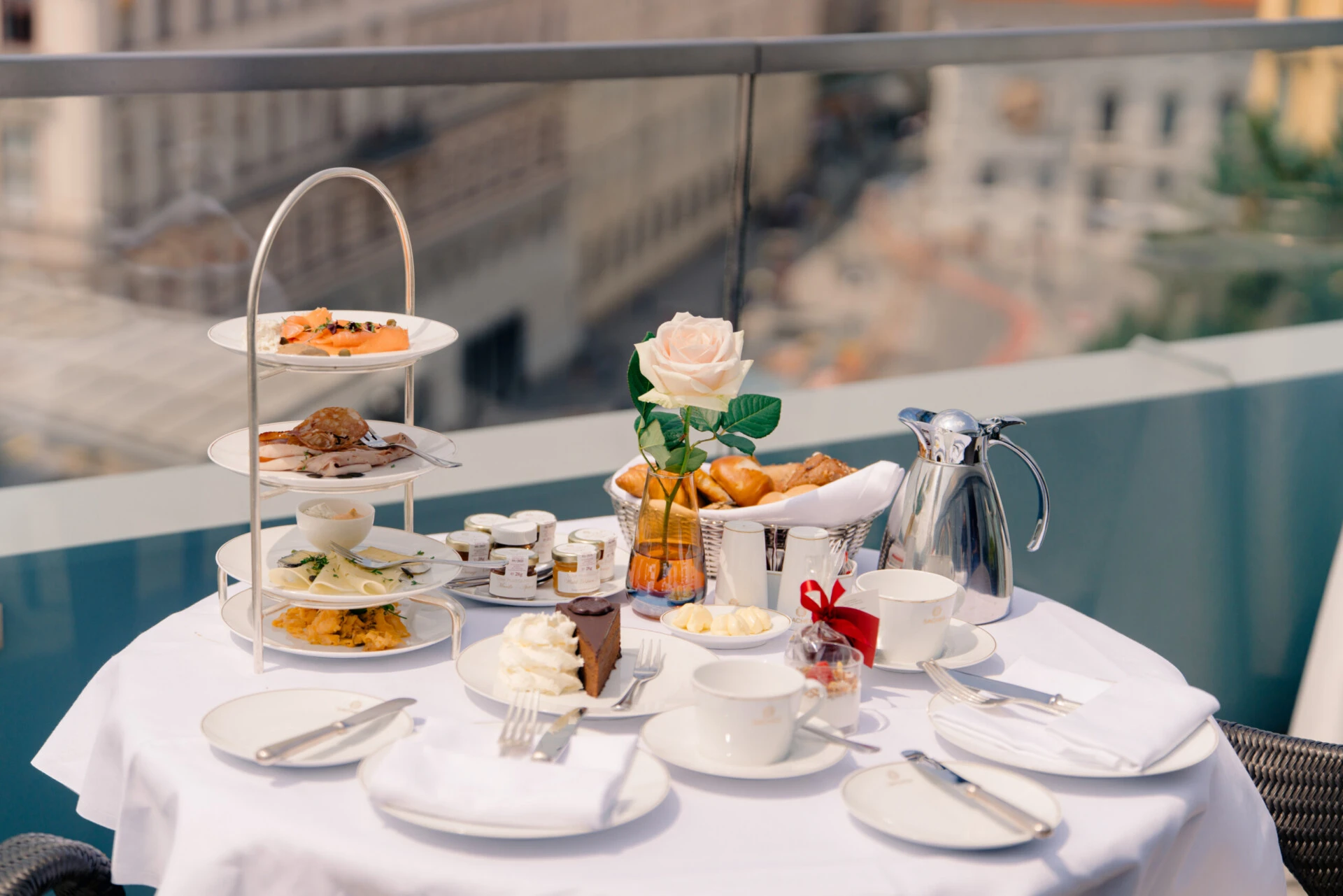 Breakfast table with Sacher-Torte, pastries, and savory dishes on a terrace at Hotel Sacher Vienna overlooking the city.