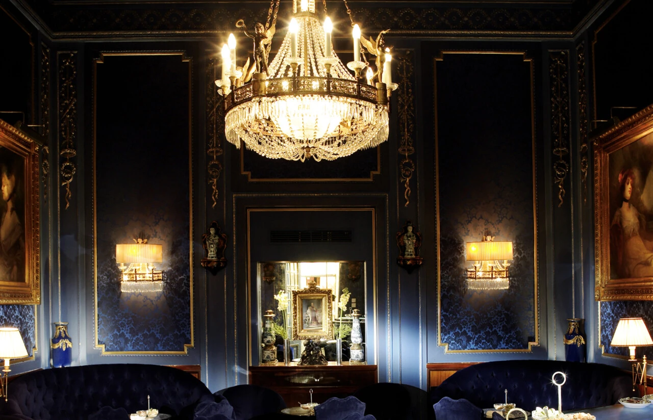 The Blaue Bar with deep blue velvet seating, ornate wallpaper, and a classical portrait in a golden frame.
