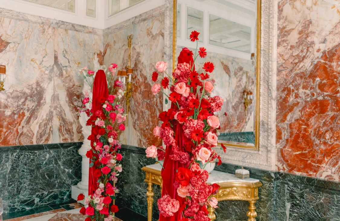 Marble Hall at Hotel Sacher Vienna with elegant marble walls, gilded details and red and pink floral arrangements.
