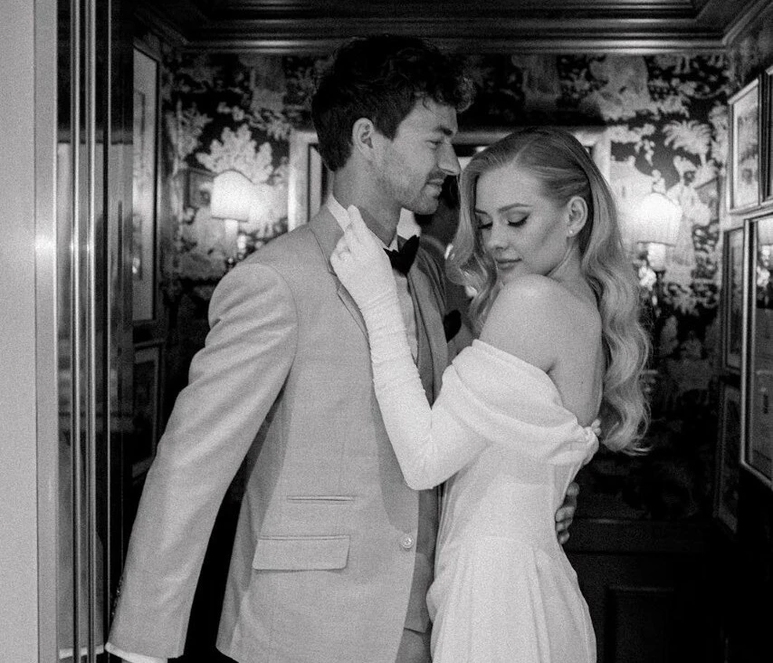 Bride and groom in elegant formalwear standing in an ornate historic interior, photographed in black and white at Hotel Sacher Vienna.
