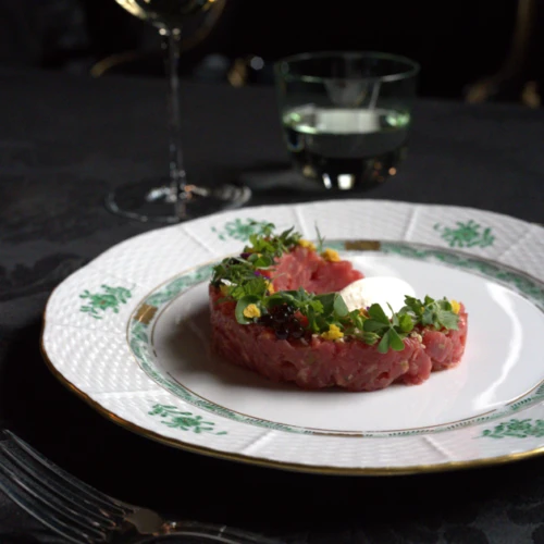 Finely plated beef tartare with herbs and caviar on elegant porcelain, served with a glass of white wine at Restaurant Grüne Bar.