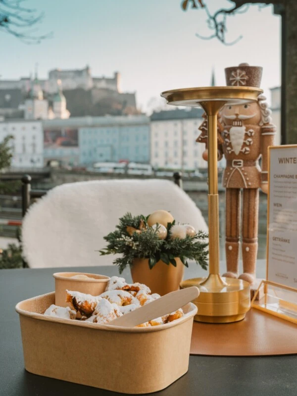 Kaiserschmarrn dusted with powdered sugar at Sacher Winter Beach in Salzburg, with festive decorations and views of Hohensalzburg Fortress.