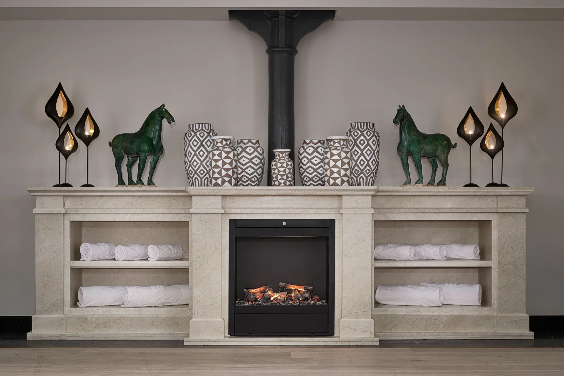 Rolled towels are neatly stored around a decorative fireplace with vases, sculptures, and ambient lighting.