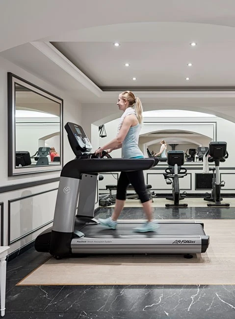 A woman exercises on a treadmill in a bright, elegant fitness room.