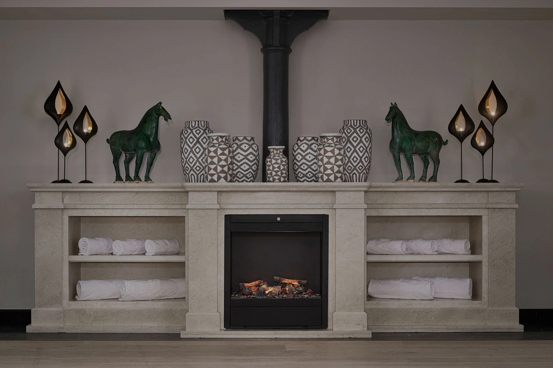 Rolled towels are neatly stored around a decorative fireplace with vases, sculptures, and ambient lighting.