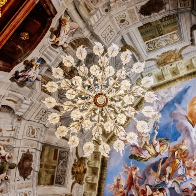 A grand chandelier hangs beneath a vibrant baroque ceiling fresco.