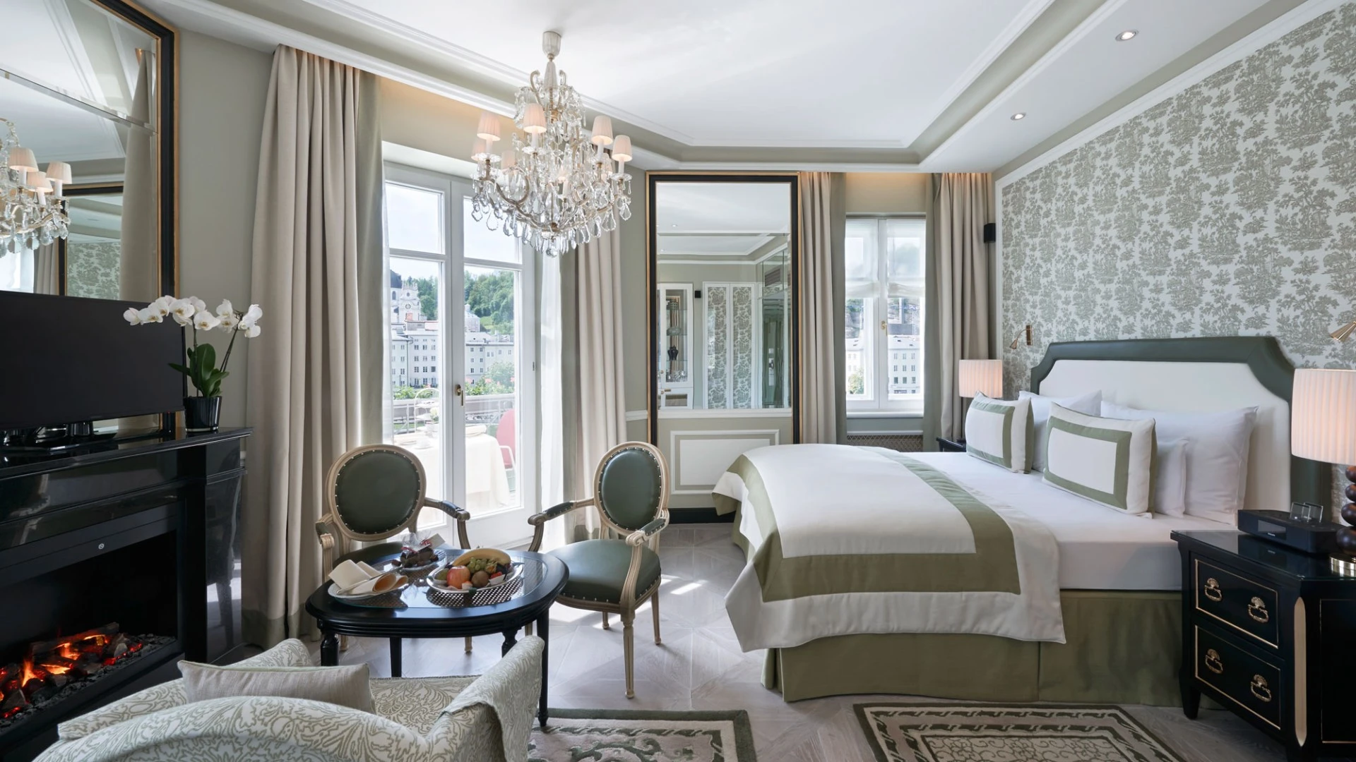 This elegant hotel room features classic decor, a crystal chandelier, and a view of Salzburg’s historic old town.
