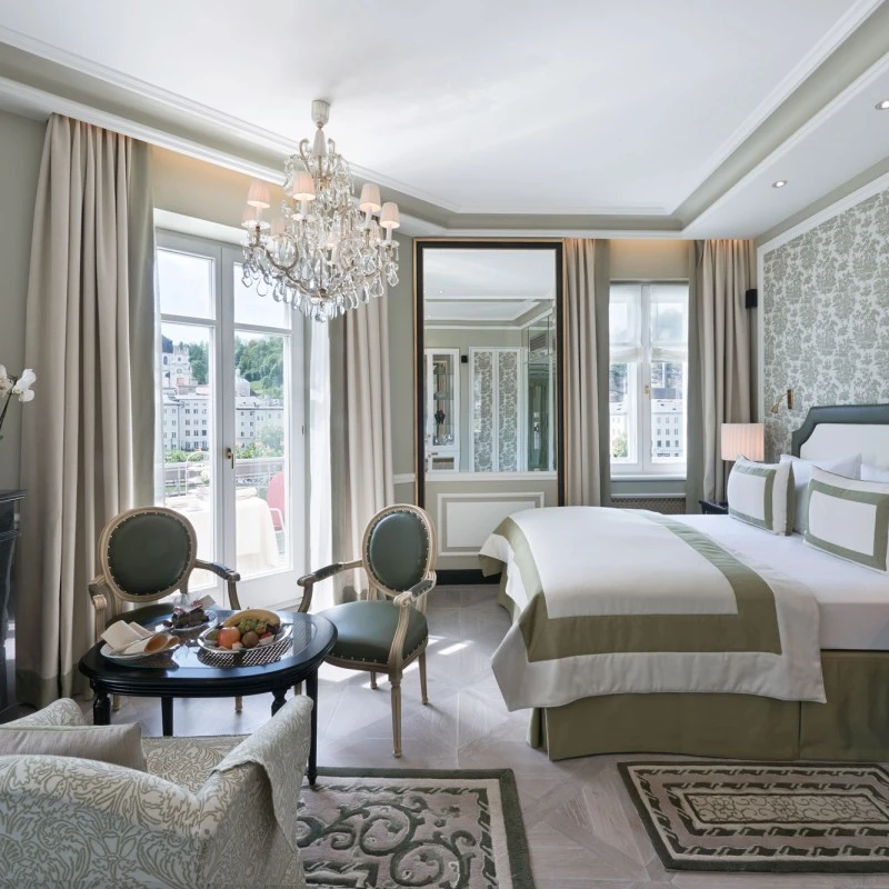 This elegant hotel room features classic decor, a crystal chandelier, and a view of Salzburg’s historic old town.