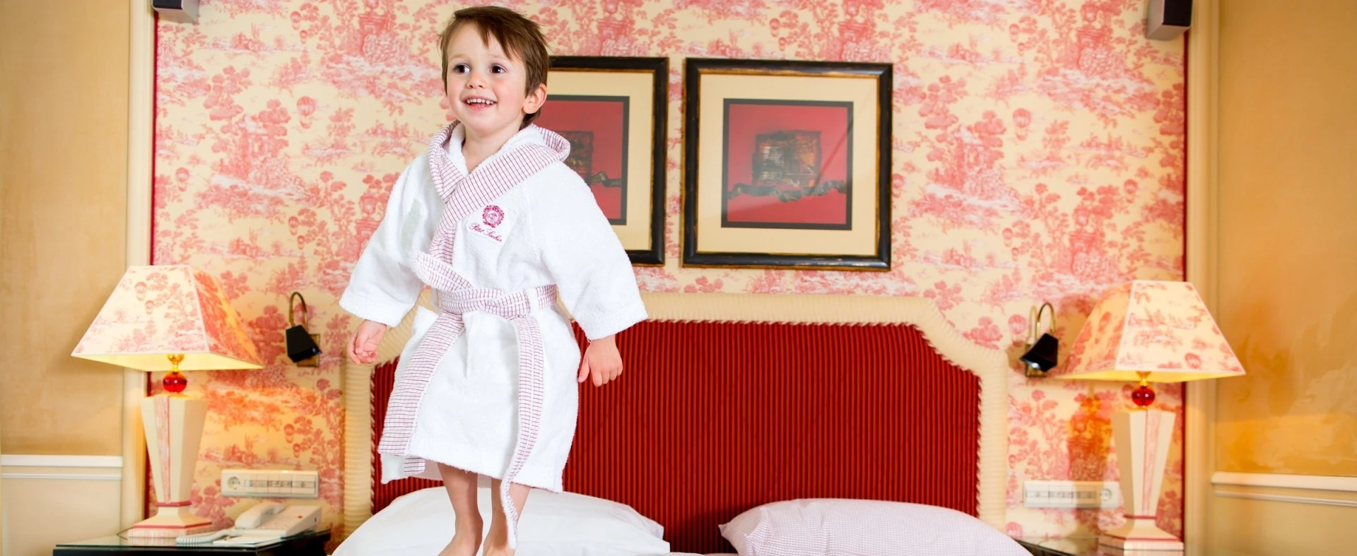Child standing on a bed in a luxury bathrobe at Petit Sacher, Hotel Sacher's family-friendly accommodations.