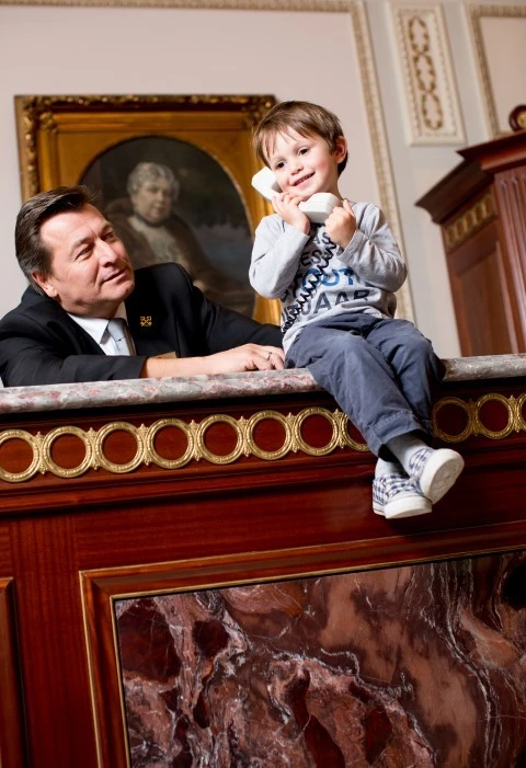 A child playfully holds a phone at a hotel counter beside a smiling concierge.