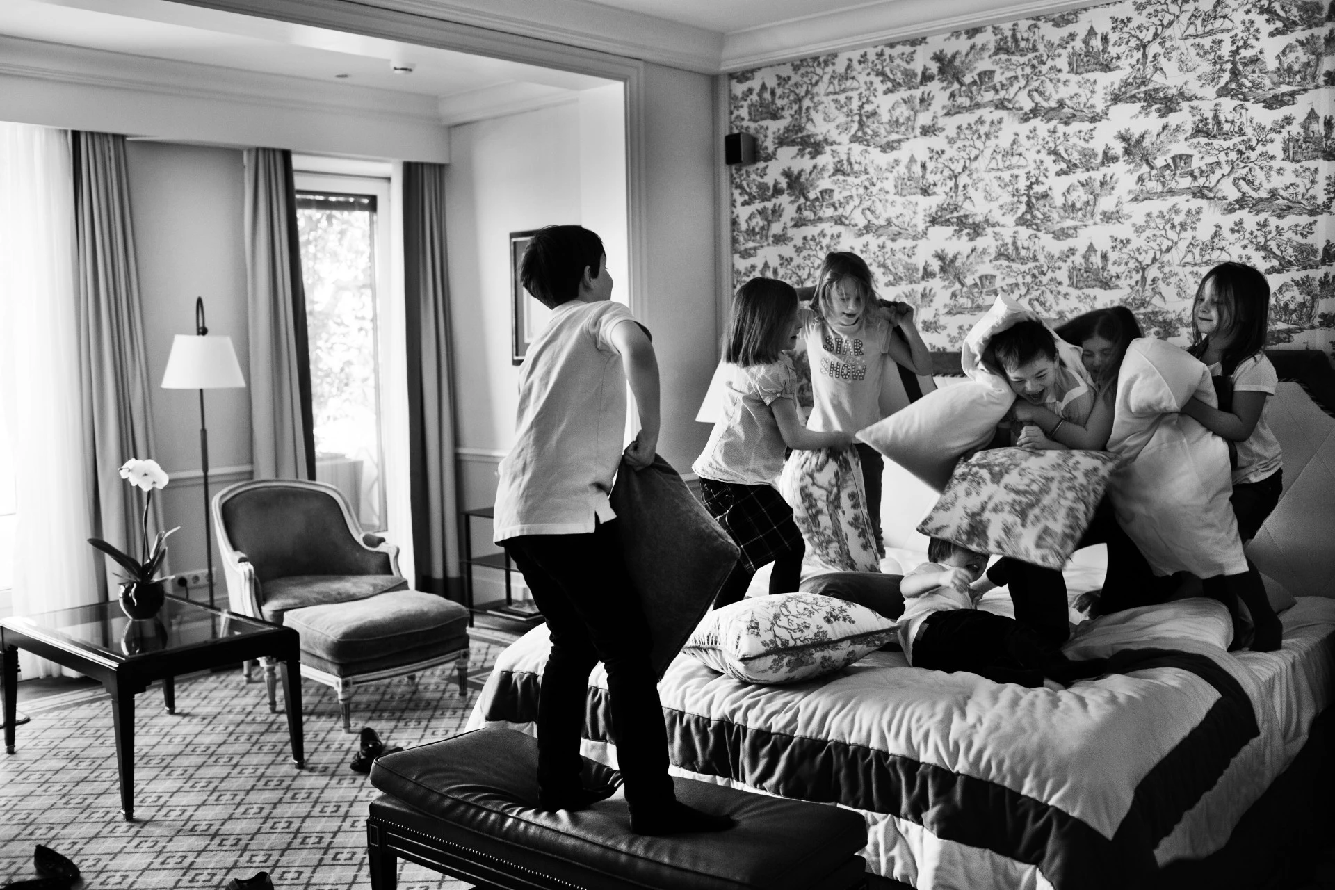 A group of children are having a playful pillow fight on a hotel bed.