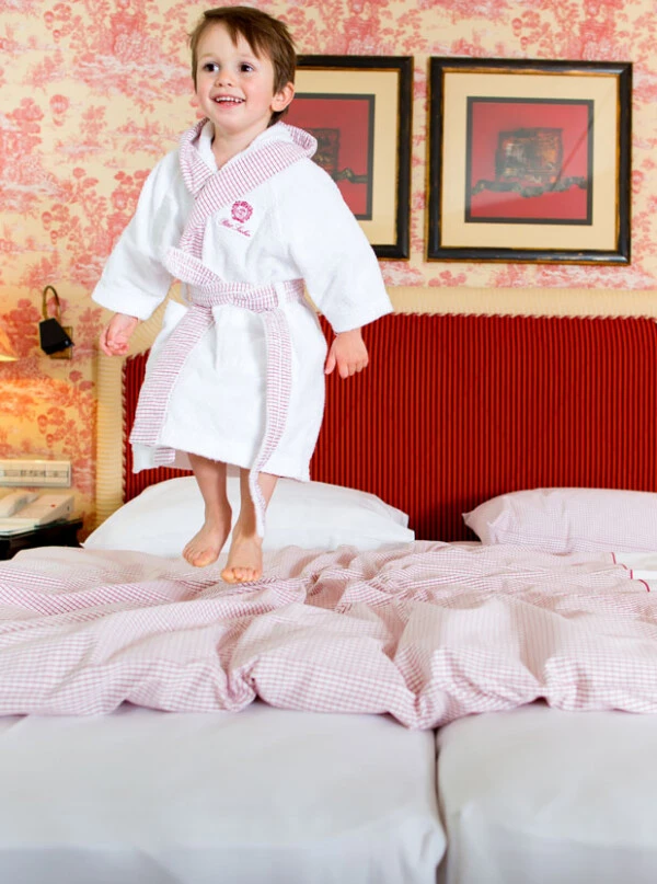 Child standing on a bed in a luxury bathrobe at Petit Sacher, Hotel Sacher's family-friendly accommodations.