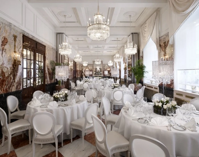 The image shows the elegant Marmorsaal (Marble Hall), featuring white-clothed tables, crystal chandeliers, and richly veined marble walls.