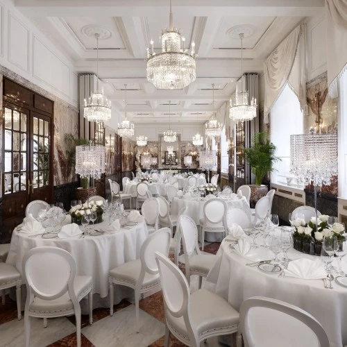 This grand dining hall features luxurious chandeliers, marble accents, and a long, elegant table setting.