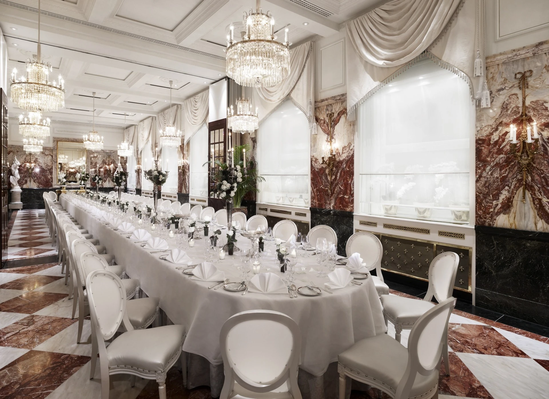 This grand dining hall features luxurious chandeliers, marble accents, and a long, elegant table setting.