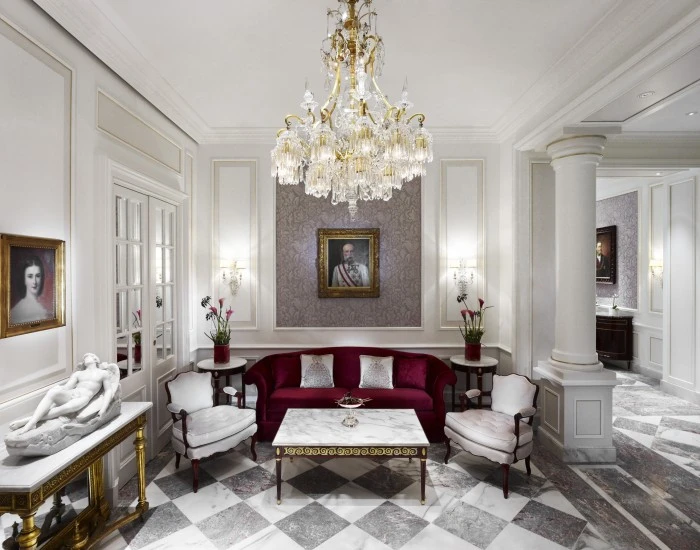 This is the Schönbrunner Loge at Hotel Sacher, an elegant lounge with imperial flair, featuring marble floors, crystal chandeliers, and portraits of Austrian royalty.