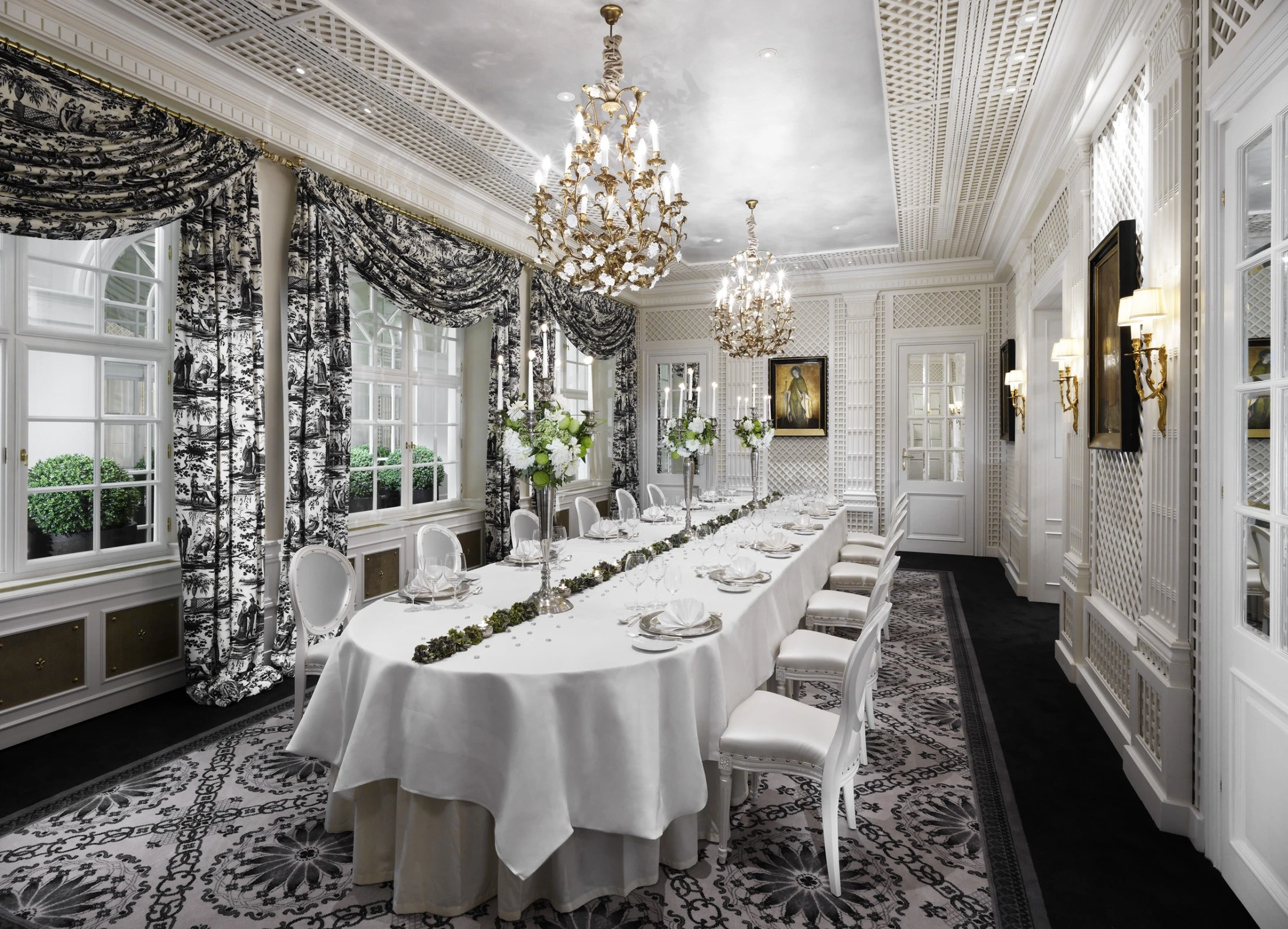 This is the Salon Metternich, an opulent dining room at Hotel Sacher Salzburg, featuring luxurious chandeliers, refined white furnishings, and richly patterned black-and-white drapery and carpets.