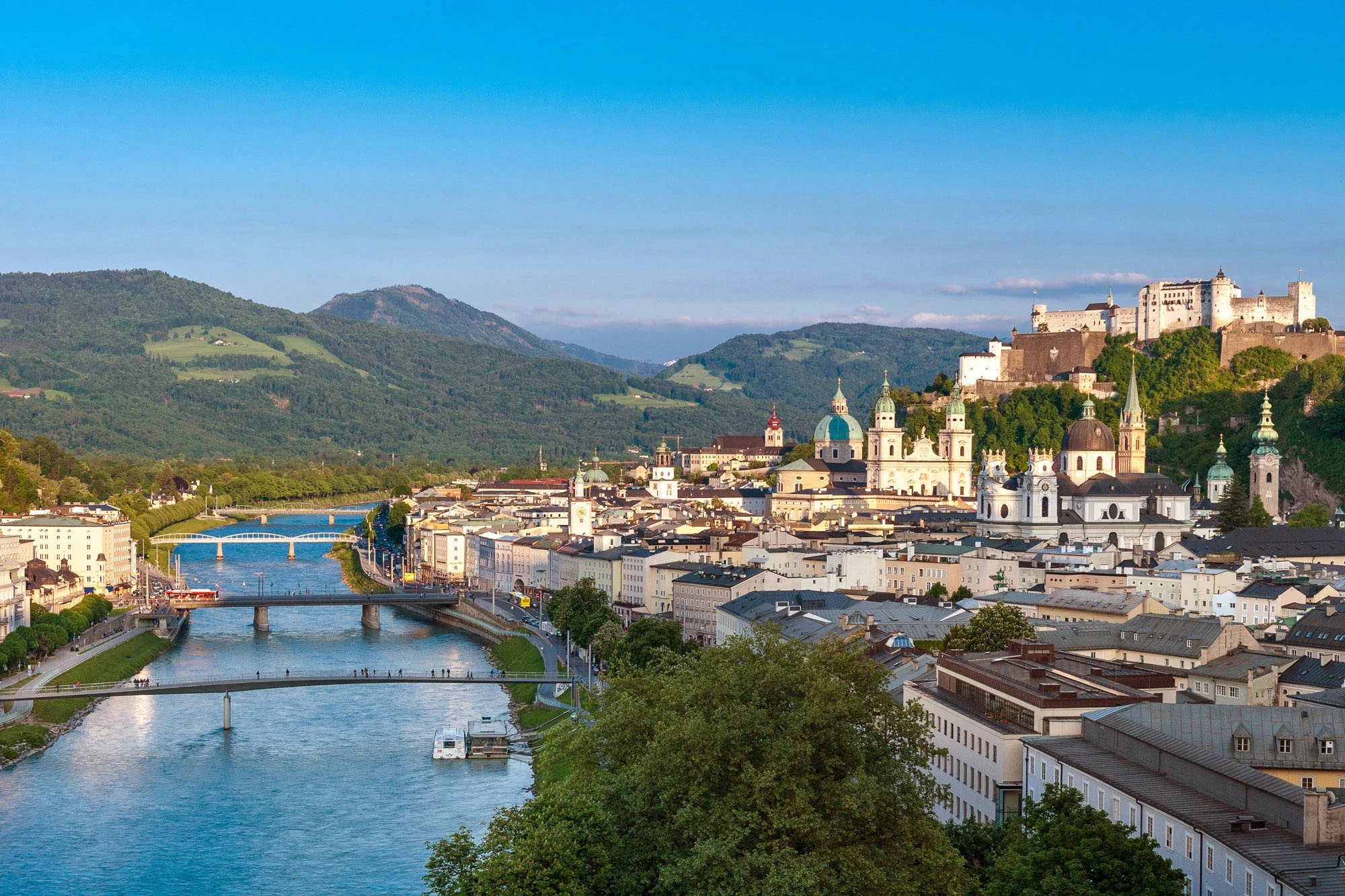 Salzburg’s skyline rises above the Salzach River, crowned by the Hohensalzburg Fortress and framed by lush hills.