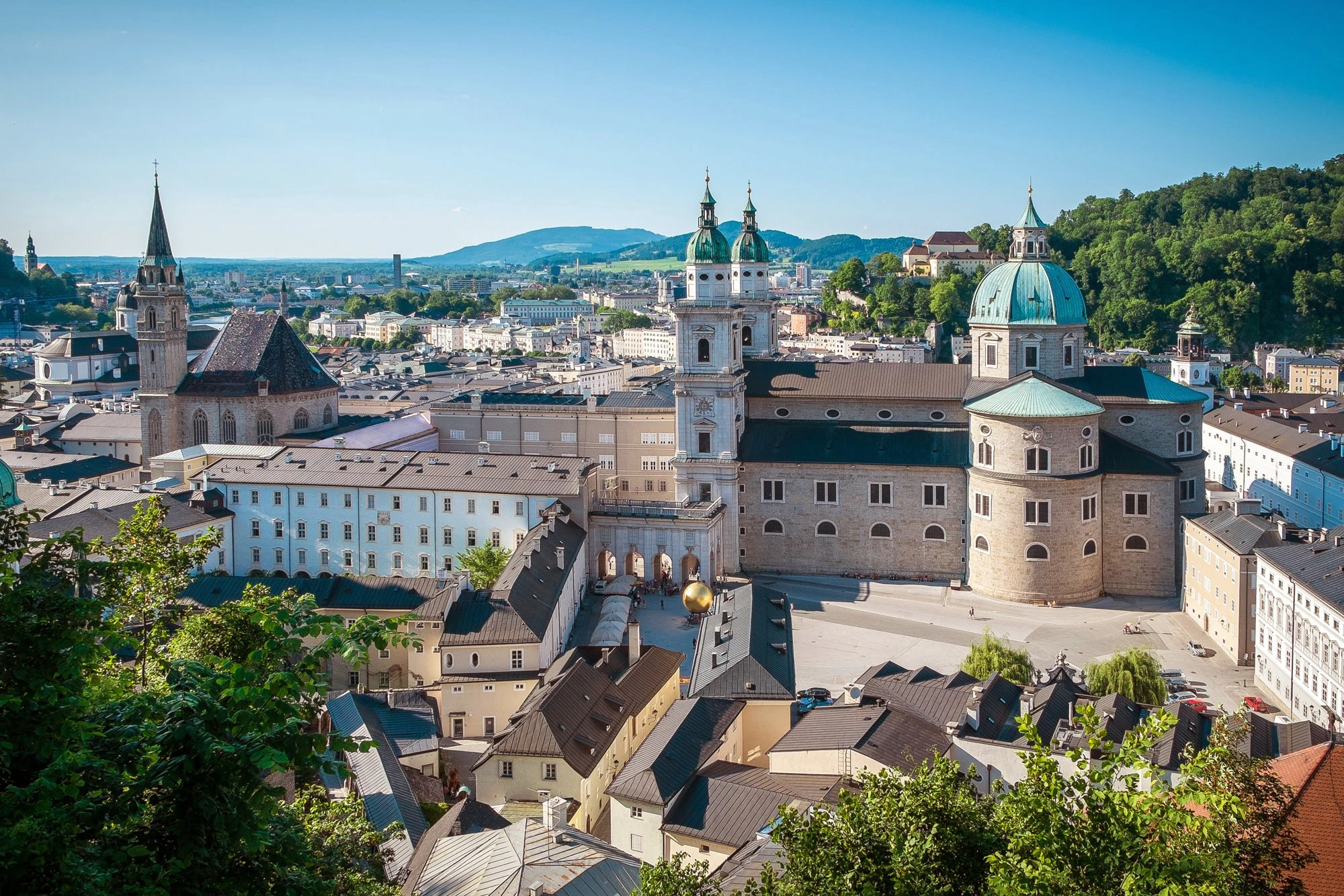 This panoramic daytime view captures the heart of Salzburg’s historic center, with the majestic DomQuartier and surrounding rooftops set against a backdrop of green hills and distant mountains.