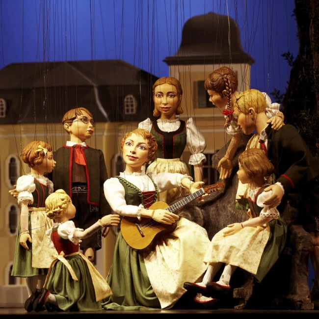 This image shows charming marionettes of Maria and the von Trapp children performing a scene from *The Sound of Music*, featured on The Original Sound of Music Tour in Salzburg.