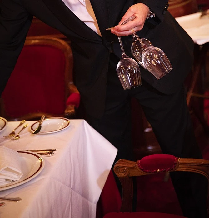 A waiter in formal attire sets a table with wine glasses in the upscale Restaurant Rote Bar.