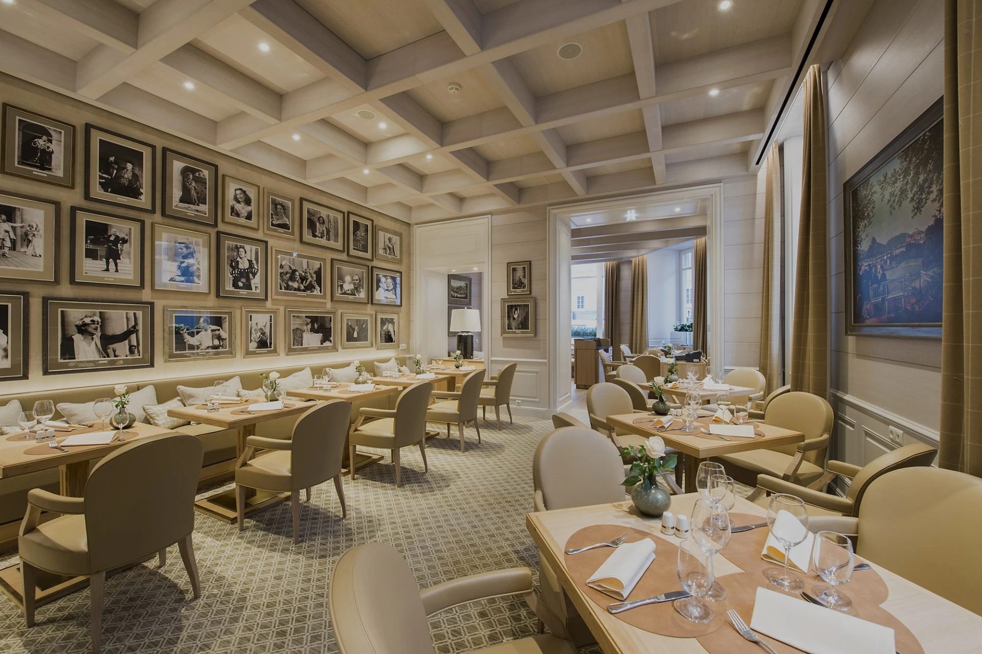 The Sacher Grill at Hotel Sacher features a bright, modern interior with light wood furnishings, elegant place settings, and a wall of black-and-white celebrity portraits.