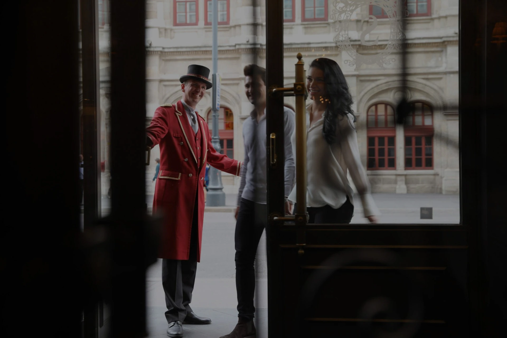 A doorman in a red coat warmly welcomes guests through the entrance of Hotel Sacher.