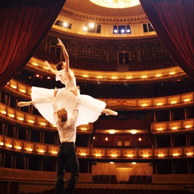 A ballerina is gracefully lifted by her partner on stage inside the grand Vienna State Opera.
