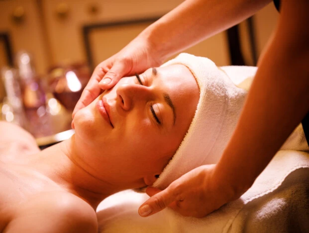 A woman enjoys a luxurious facial massage in a serene spa setting, wrapped in soft towels and basking in the warm ambient lighting.