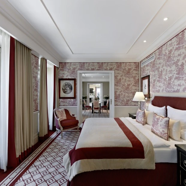 A luxurious bedroom with classic red and cream toile wallpaper, elegant furnishings, and access to a private terrace.