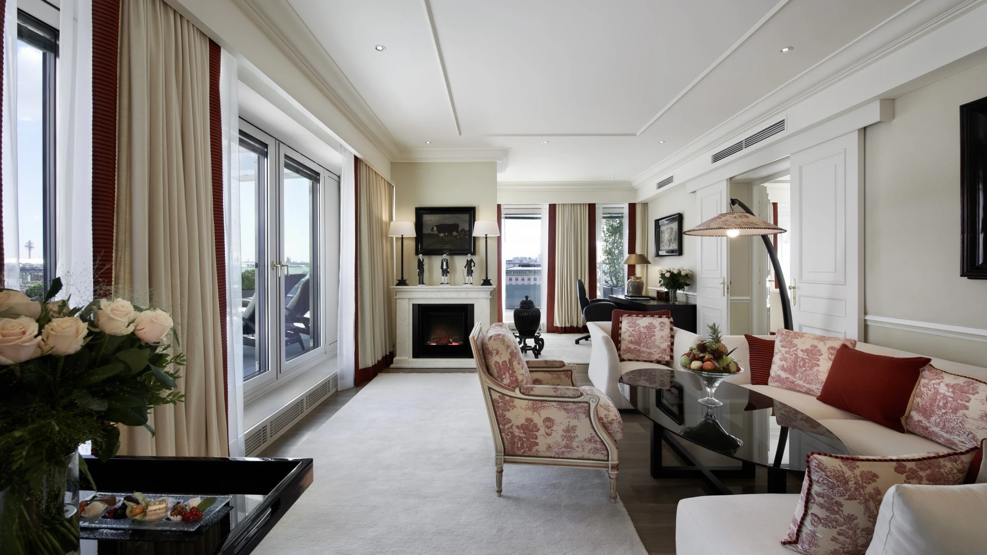 A refined, light-filled suite featuring elegant floral upholstery, a modern fireplace, and access to a private terrace with city views.