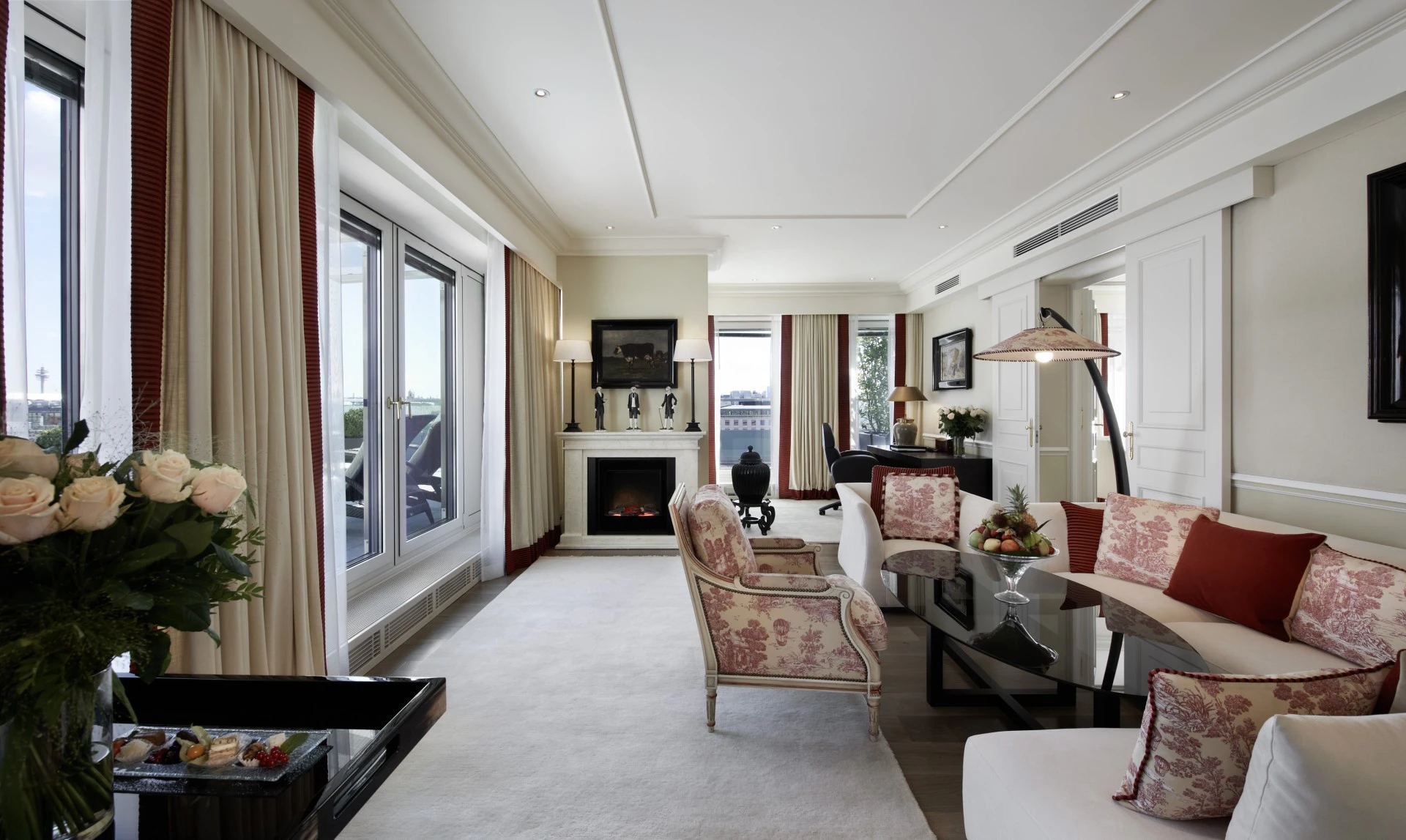A refined, light-filled suite featuring elegant floral upholstery, a modern fireplace, and access to a private terrace with city views.