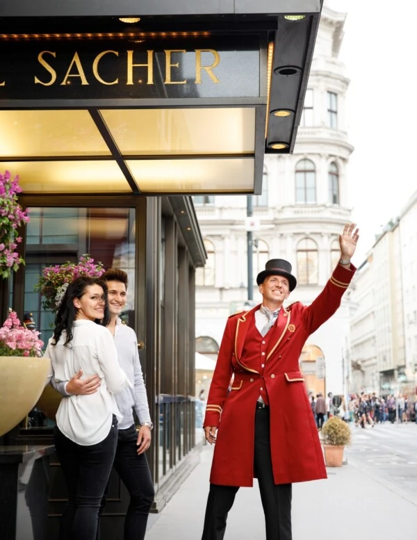 A doorman in red livery warmly greets guests outside Hotel Sacher in Vienna.