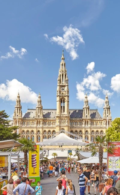 Crowds enjoy a summer festival in front of Vienna’s grand Rathaus under a clear blue sky.