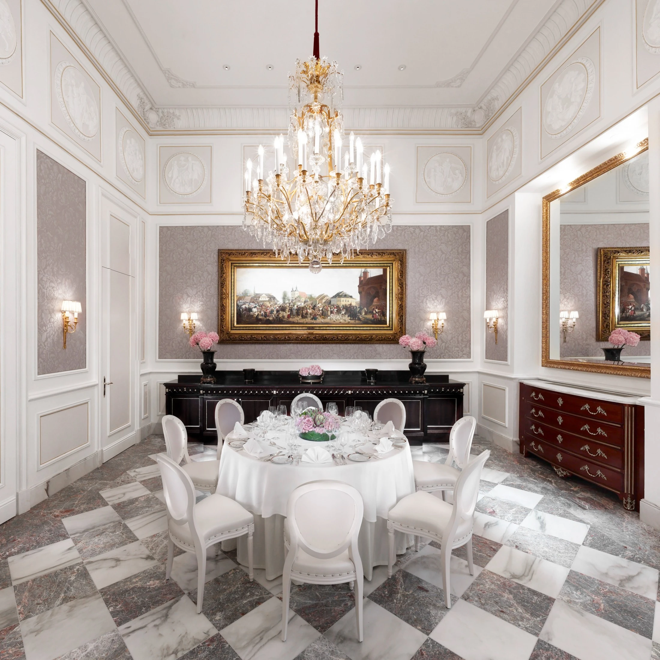 The elegant Salon Mayerling features a grand chandelier, classical decor, and a round table set for fine dining.