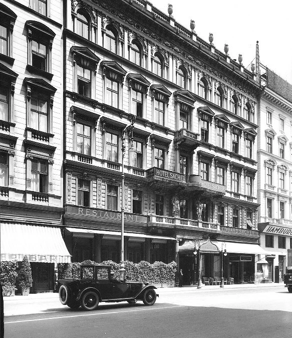 A historic view of the Hotel Sacher building with a vintage car parked in front.